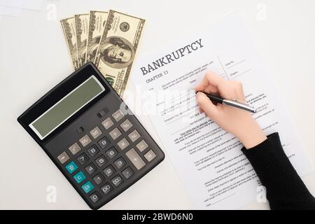 vue rognée de la femme remplissant la forme de faillite avec stylo près de l'argent et calculatrice sur fond blanc Banque D'Images