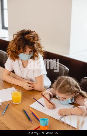 mère dans un masque médical regardant le dessin d'enfant à la maison Banque D'Images