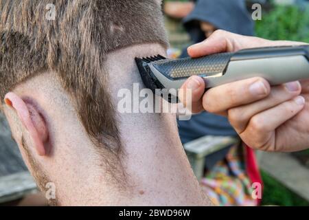 Un homme tente de couper les cheveux d'un autre homme pendant le verrouillage du coronavirus lorsque les coiffeurs sont fermés, laissant la queue d'un rat d'un côté de la tête Banque D'Images