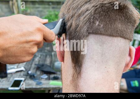 Un homme tente de couper les cheveux d'un autre homme pendant le verrouillage du coronavirus lorsque les coiffeurs sont fermés, laissant la queue d'un rat d'un côté de la tête Banque D'Images