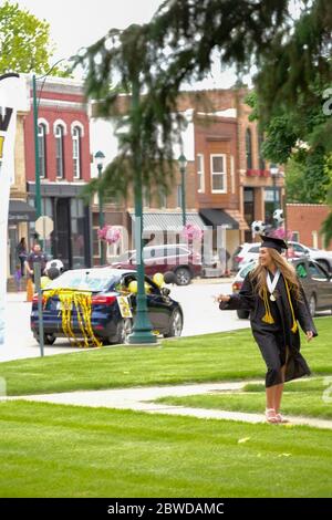 Winterset, Iowa, États-Unis. 31 mai 2020. Un senior de l'école secondaire Winterset fait des gestes à sa famille sur le trottoir vers les marches du palais de justice du comté de Madison pour recevoir son diplôme lors d'une cérémonie de remise des diplômes de conduite le 31 mai 2020. Les diplômés et leurs familles ont reçu deux véhicules chacun et ont reçu des blocs de temps par ordre alphabétique. Après avoir parcouru une rue fermée, les aînés ont marché jusqu'aux marches du palais de justice du comté de Madison pour recevoir la reconnaissance et leur diplôme des responsables scolaires. Les écoles Winterset ont indiqué que 146 élèves étaient admissibles à un diplôme. (Image crédit : © Fritz Norde Banque D'Images