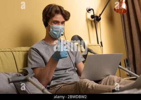 Concentration sélective de l'homme handicapé dans le casque et masque médical montrant comme pendant le chat vidéo sur ordinateur portable à la maison Banque D'Images