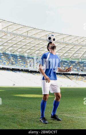 joueur de football professionnel en uniforme bleu et blanc avec ballon sur la tête au stade Banque D'Images