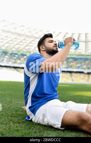 joueur de football professionnel en uniforme bleu et blanc assis sur le terrain de football et de l'eau potable au stade Banque D'Images