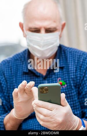 Paris, France - Mars 2020: Homme senior portant des gants de protection en plastique et un masque respiratoire médical chirurgical pendant l'isolement mondial du coronavirus à l'aide d'un smartphone Apple iPhone 11 Pro Banque D'Images