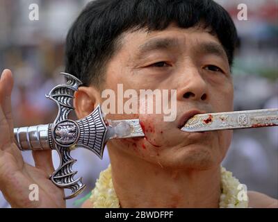 Le dévot taoïste chinois thaïlandais pière sa joue droite avec une épée traditionnelle pendant le Festival végétarien de Phuket (Festival des neuf dieux des Empereurs). Banque D'Images