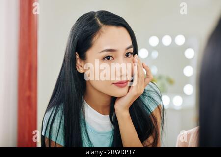 Belle jeune femme vietnamienne appliquant sous la crème des yeux pour les cercles sombres Banque D'Images