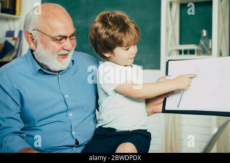 Portrait du grand-père et du petit-fils sur un tableau noir en classe. Enfant avec un vieux professeur apprenant en classe sur fond de tableau noir. Père et fils. Banque D'Images