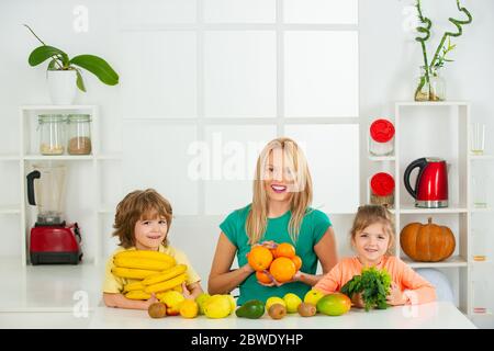 Maman fille et fils préparent un smoothie dans la cuisine. Famille heureuse et aimante. Amusez-vous et jouez avec les légumes. Une alimentation saine et un mode de vie sain pour les enfants. Banque D'Images