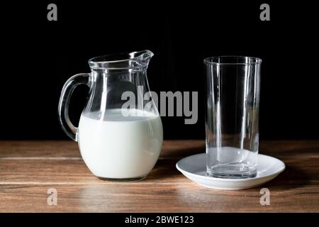 Une tasse en verre vide et un pot de lait de vache sur une table en bois Banque D'Images