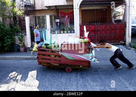 Antipolo City, Philippines - 28 mai 2020 : le vendeur de rue pousse son chariot rempli de noix de coco fraîches le long d'une route en pente ascendante. Banque D'Images