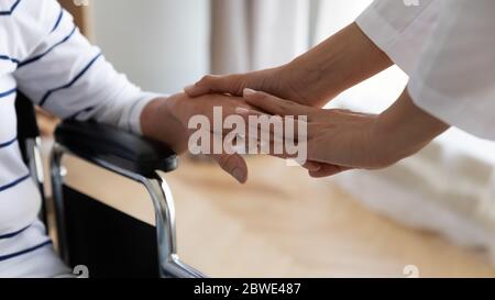 Femme âgée handicapée assise en fauteuil roulant, sa paume tenant une infirmière Banque D'Images