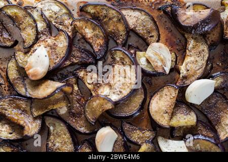 Tranches d'aubergines cuites au four avec gousses d'ail couchées sur un plateau en verre prêt à être mangé Banque D'Images