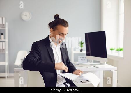 Un homme brunette dans une veste noire assise à la table travaille avec des papiers au bureau. Banque D'Images