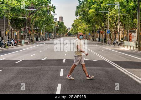 Homme portant un masque chirurgical en traversant une avenue vide Passeig de Gracia pendant la pandémie de Covid-19, Barcelone, Catalogne, Espagne Banque D'Images