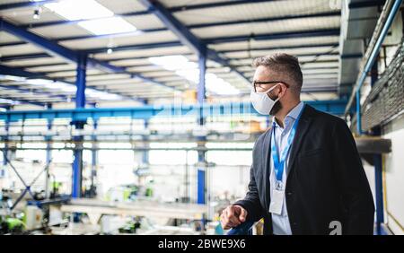 Technicien ou ingénieur avec masque de protection debout en usine. Banque D'Images