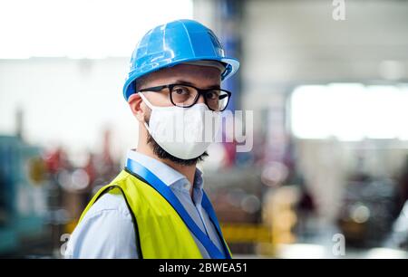 Technicien ou ingénieur avec masque de protection et casque debout en usine. Banque D'Images