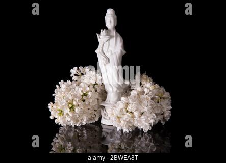 Guanyin encadré de fleurs de lilas blanc sur fond noir avec réflexion Banque D'Images