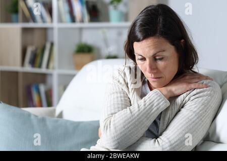 Triste femme d'âge moyen pensive regardant vers le bas dépresed assis sur le canapé dans le salon à la maison Banque D'Images