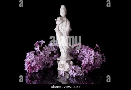 Guanyin encadré de fleurs de lilas roses sur fond noir avec réflexion Banque D'Images