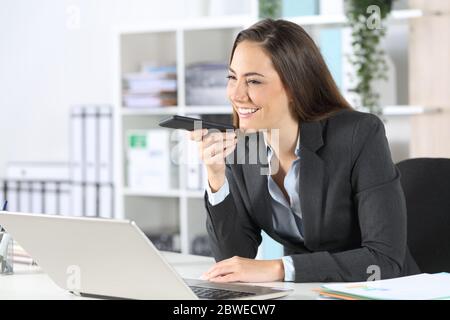 Heureuse femme dirigeante utilisant le système de reconnaissance vocale sur un smartphone assis sur un bureau au bureau Banque D'Images