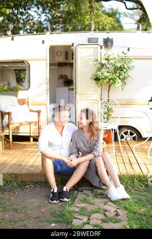 Jeune couple européen assis près de la maison sur roues et embrassant. Banque D'Images