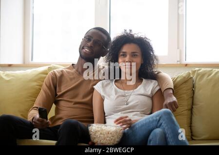 Couple assis sur un canapé en train de manger du pop-corn en regardant des films à la télévision Banque D'Images