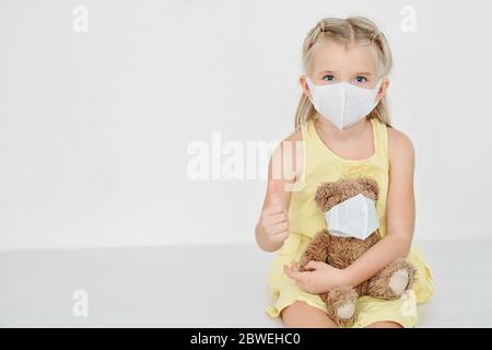 Petite fille avec un masque médical sur son visage et le visage de son ours en peluche montrant le pouce vers le haut Banque D'Images