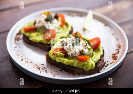 Écrasée de toasts d'avocat avec des tomates cerises et du fromage féta émietté sur une assiette de pain de seigle. Concept d'alimentation saine. Banque D'Images