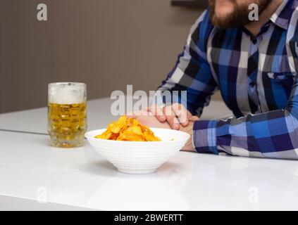 L'homme barbu boit de la bière et mange des frites dans la cuisine, de la nourriture de mauvaise qualité, de la convivialité Banque D'Images