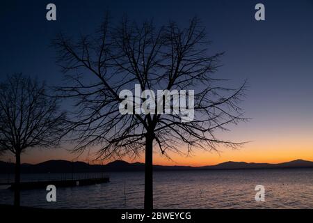 Coucher de soleil sur le lac Trasimène en Ombrie, Italie, avec des arbres contre la lumière Banque D'Images