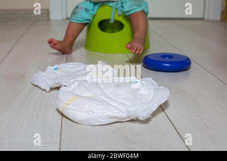 concept d'entraînement en pot. gros plan un couches est sur un sol blanc, en arrière-plan un joli petit bébé est assis sur un pot vert avec jouet dans la pièce dans le flou Banque D'Images