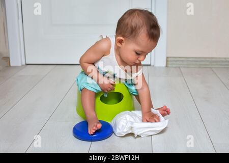 concept de formation de pot. Un bébé mignon est assis sur un pot vert et joue avec un couches dans la chambre. Gros plan, mise au point douce, place pour le photocopieur Banque D'Images