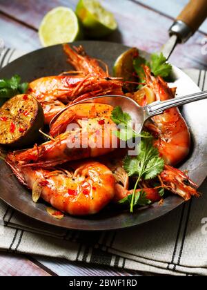 Décorez les crevettes dans une poêle avec du Chili, de l'ail, de la coriandre et de la lime sur une table en bois et une serviette de table Banque D'Images