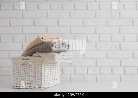 Serviettes fraîches multicolores dans un panier en paille d'osier sur une table blanche avec un mur en brique blanche sur toile de fond. Banque D'Images