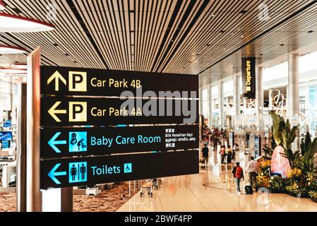 Singapour, aéroport de Changi, novembre 19 : intérieur moderne du terminal 4 rempli de touristes. Panneau indiquant les directions vers le parking, les toilettes et les services de garde d'enfants Banque D'Images