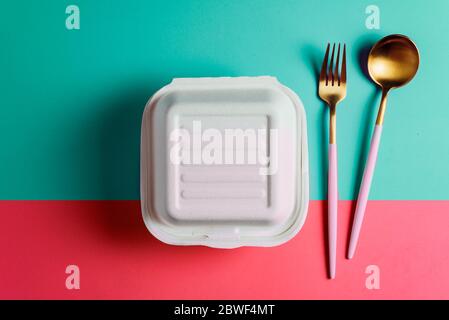 Concept de nourriture saine : emballage blanc en burguer fermé avec une fourchette et une cuillère dorées, dans une boîte à lunch en carton à emporter au bureau sur une surface rose Banque D'Images