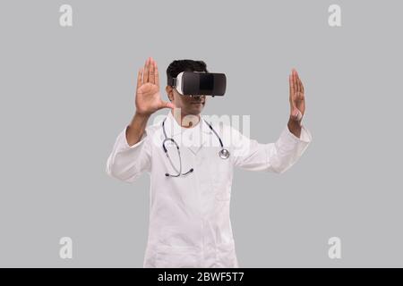 Médecin portant des lunettes VR mains sur les côtés isolé. Indian Man Doctor pointant dans la réalité virtuelle Banque D'Images