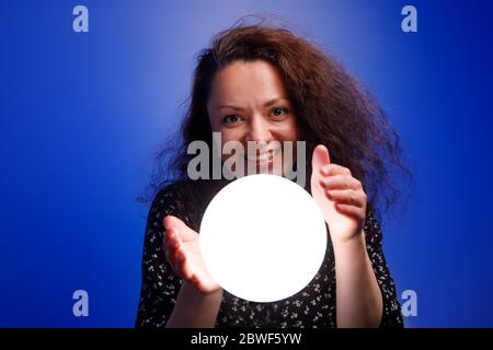 Fille souriante tenant une balle brillante dans ses mains. Arrière-plan bleu. Banque D'Images