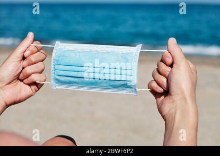 gros plan d'un jeune homme caucasien avec un masque chirurgical bleu dans ses mains sur la plage Banque D'Images