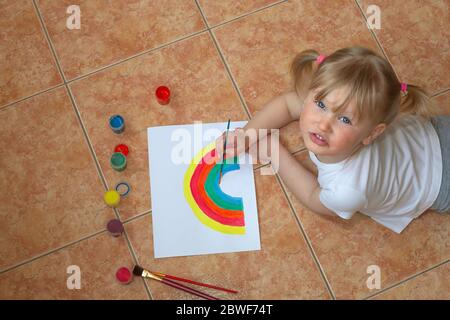 Petite fille dessin arc-en-ciel. Signe d'espoir pendant l'éclosion du coronavirus. Mise en quarantaine amusante. Arts et artisanat pour les enfants. Peinture pour enfants. École enfant faisant art maison Banque D'Images