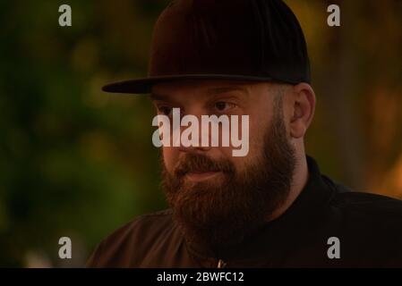 Homme avec une barbe sur un fond de verdure.UN gars avec une barbe noire dans une casquette de baseball noire.l'homme est tiré au coucher du soleil. Banque D'Images