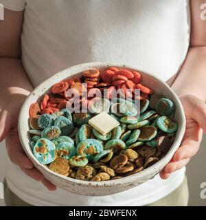 Plats tendance - céréales à crêpes. Mini crêpes aux céréales colorées dans un bol entre les mains des enfants. Les enfants tiennent de petites crêpes avec un colorant naturel - matcha vert, spiruline de dinde, pois bleus, fruit de dragon rouge Banque D'Images