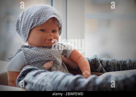 Les mains de la fille prennent la poupée hors de la boîte. Poupée dans une sunress grise et foulard sur un fond clair. Banque D'Images