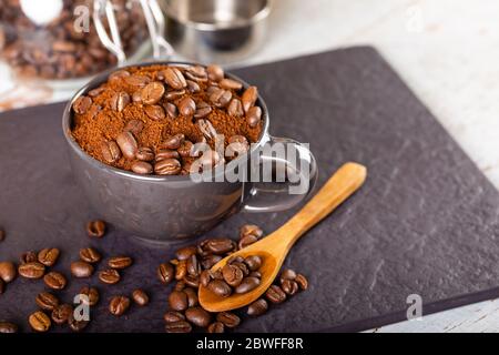 Café noir moulu dans une tasse noire et plusieurs grains de café torréfiés sur le dessus. Banque D'Images