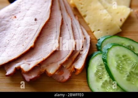 Trancher du jambon, des concombres et du fromage avec des pains fins et grossiers se trouvent sur une planche en bois. Banque D'Images