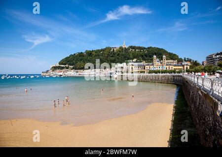 Vue sur la promenade de la plage à San Sebastian, Espagne occupé avec des gens lors d'une journée ensoleillée avec des bateaux amarrés dans la baie. Banque D'Images