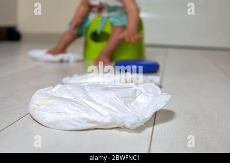 concept d'entraînement en pot. gros plan un couches est sur un sol blanc, en arrière-plan un joli petit bébé est assis sur un pot vert avec jouet dans la pièce dans le flou Banque D'Images