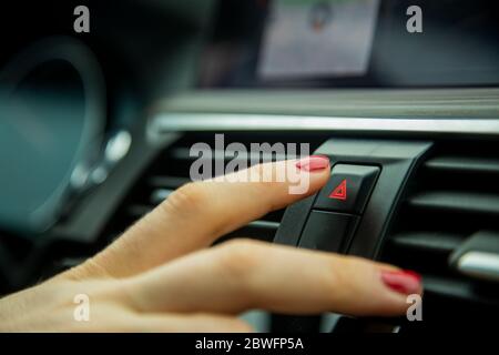 une femme appuie sur le bouton de la lumière d'urgence sur le tableau de bord d'une voiture. gros plan, mise au point douce, en arrière-plan intérieur de voiture détails en flou, côté Banque D'Images