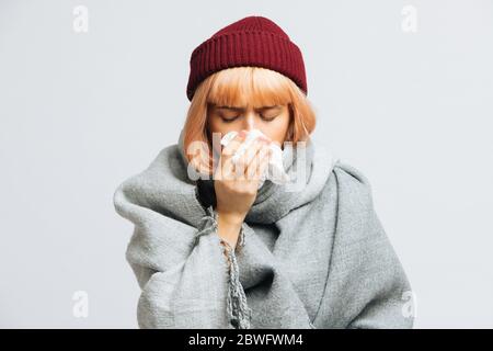 Jeune femme malsaine en chapeau rouge, écharpe chaude avec serviette en papier éternuant, éprouve des symptômes d'allergie, attrapé un froid, les yeux fermés. Mal désespéré woma Banque D'Images